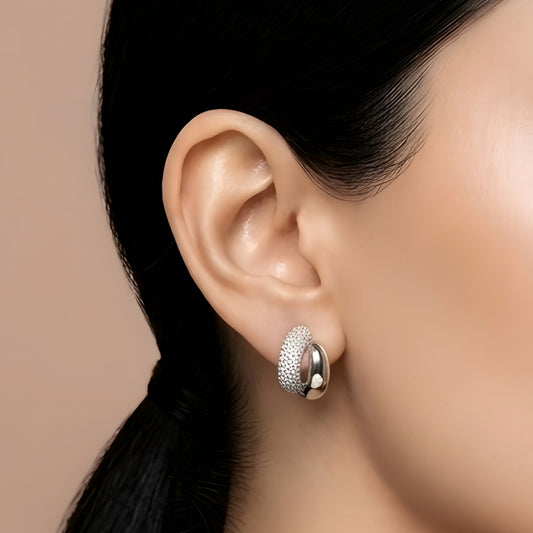 Silver toned anti tarnish pave stud earrings with dual finish and sparkling stone detailing worn on ear.
