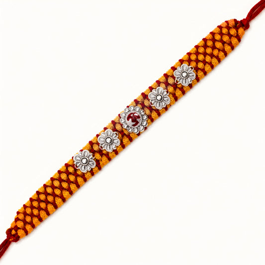 Sterling Silver Om Floral Mauli Rakhi with red enamel Om centrepiece, silver flower motifs and saffron red woven thread