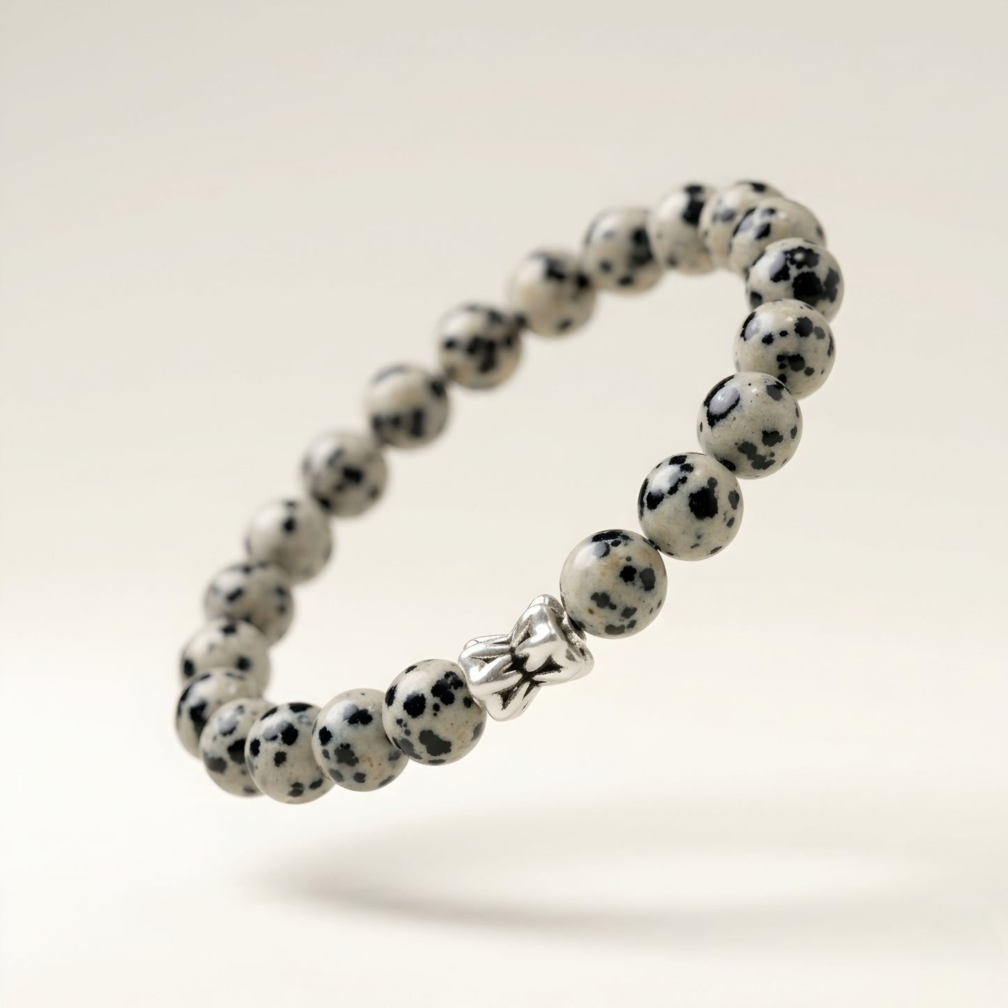 Natural Dalmatian Jasper bracelet featuring 8 mm cream and black speckled gemstone beads with a butterfly accent bead on a smooth stone background.