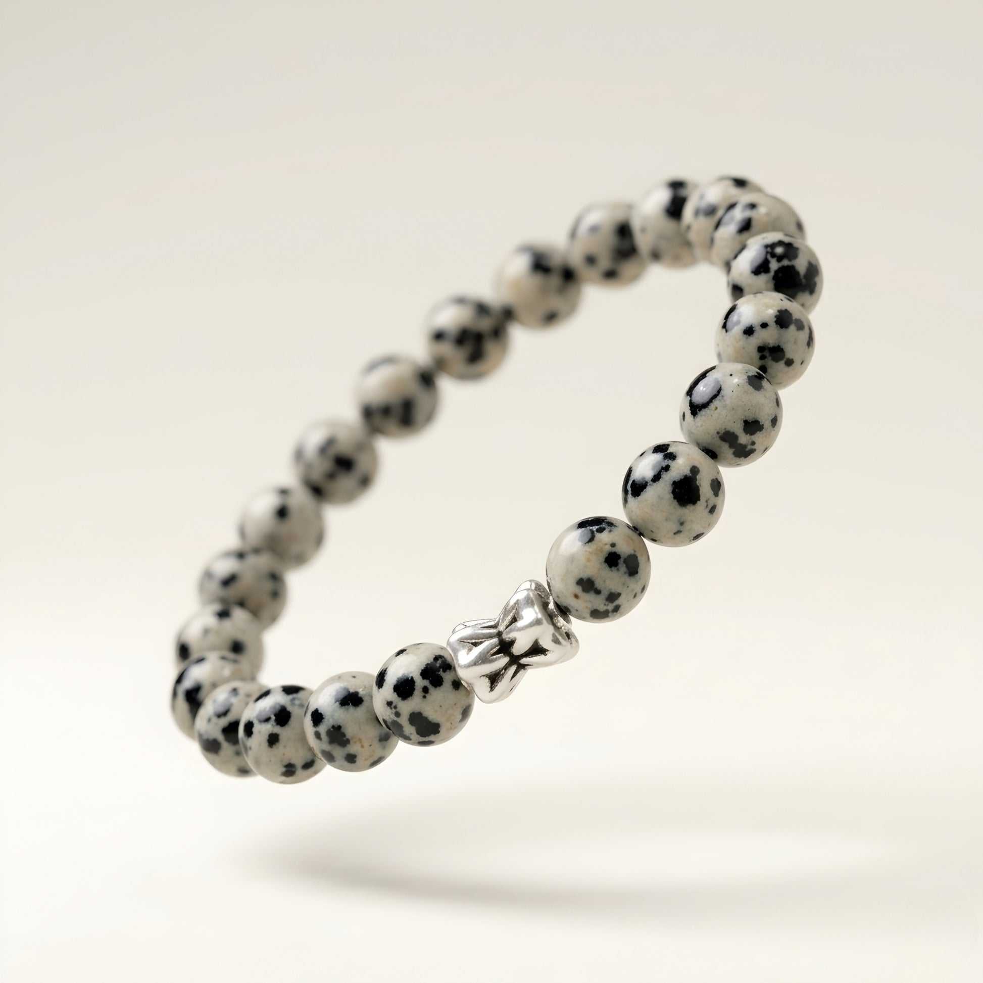 Natural Dalmatian Jasper bracelet featuring 8 mm cream and black speckled gemstone beads with a butterfly accent bead on a smooth stone background.