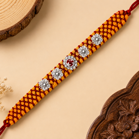 Sterling Silver Om Floral Mauli Rakhi with red enamel Om centrepiece, silver flower motifs and saffron red woven thread