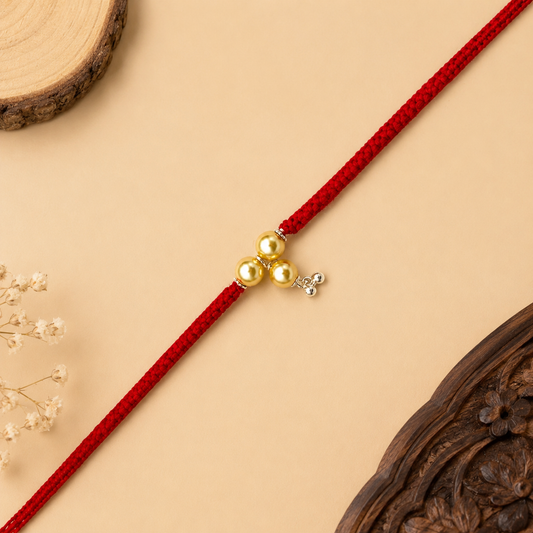 Sterling Silver Bhabhi Rakhi with three gold-tone beads, small silver hanging charm and red woven thread