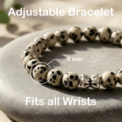 Natural Dalmatian Jasper bracelet featuring 8 mm cream and black speckled gemstone beads with a butterfly accent bead on a smooth stone background.